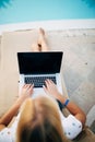 Attractive young woman in sunglasses is lying on a chaise-lounge near swimming pool with laptop. Royalty Free Stock Photo