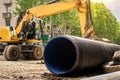 Working excavator on the roadway street. Close-up of large plastic corrugated pipe for water supply against the background of Royalty Free Stock Photo