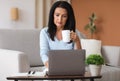 Mature woman sitting on sofa drinking coffe working on computer Royalty Free Stock Photo