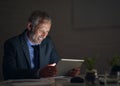 Working late made worthwhile. Shot of a mature businessman using a digital tablet while working late in an office.