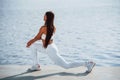 Working on the legs. Shot of sportive woman doing fitness exercises near the lake at daytime