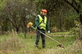 A working man in professional outfit mows grass with a trimmer, a mower. Mowing lawns, roadsides, edge