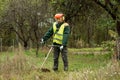 A working man in professional outfit mows grass with a trimmer, a mower. Mowing lawns, roadsides, edge Royalty Free Stock Photo