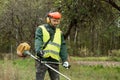 A working man in professional outfit mows grass with a trimmer, a mower. Mowing lawns, roadsides, edge