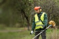 A working man in professional outfit mows grass with a trimmer, a mower. Mowing lawns, roadsides, edge Royalty Free Stock Photo