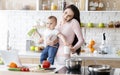 Young mom talking on phone and holding baby at kitchen