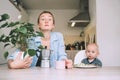 Working mother with little baby. Young tired woman with coffee and baby having breakfast in kitchen. Modern freelancer mom and her Royalty Free Stock Photo