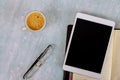 Working at office desk using a digital tablet with porcelain cup of black coffee, eyeglasses, notebook weekly