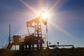 Working oil pump silhouette against sun and blue sky