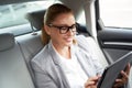 Working online. Successful business woman using digital tablet and smiling while sitting on back seat in the car. On the Royalty Free Stock Photo