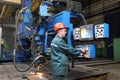 Working operator controls welding robot, standing at control pan