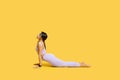 Working out. Young black woman practicing yoga, doing Cobra exercise, staying in Bhujangasana pose, yellow background Royalty Free Stock Photo