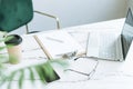 Working place with paper cup of coffee, notes, open laptop, eye glasses and smartphone on white marble table in bright modern Royalty Free Stock Photo