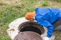 A working plumber bent over a water well to inspect pipes and a meter. Rural water supply, repair and maintenance Royalty Free Stock Photo