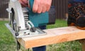 Working with a power tool. A builder is sawing a board at the construction site of a new house. Close-up on gloved hands holding a