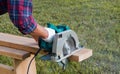 Working with a power tool. A builder is sawing a board at the construction site of a new house. Close-up on gloved hands holding a