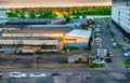 Evening, working production facilities, a car, a residential multi-storey building next door, a forest in the distance and a lake