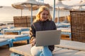 Working remotely on seashore. Young successful woman female freelancer in straw hat working on laptop while sitting on