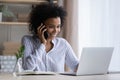Black female office employee multitasking talking by phone using laptop Royalty Free Stock Photo