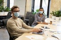 Working safely. Male and female office workers wearing medical protective masks sitting together at the table in the