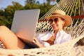 Working at sunset. Side view of young happy female using laptop while lying in the hammock on the beach Royalty Free Stock Photo