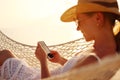 Working at sunset. Young happy female using smartphone while lying in the hammock on the beach Royalty Free Stock Photo