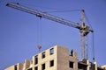 Working tall cranes inside place for with tall buildings under construction against a clear blue sky. Crane and building working