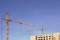 Working tall cranes inside place for with tall buildings under construction against a clear blue sky. Crane and building working Royalty Free Stock Photo