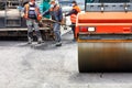 The working team of road workers in protective medical masks and overalls lay a new asphalt coating to the work site