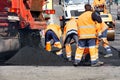 The working team scatters a part of the asphalt with shovels to repair a section of the road