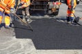 The working team smoothes hot asphalt with shovels by hand when repairing the road