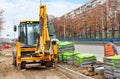 An orange road excavator works at a work site paving paving slabs along a city street on a spring afternoon