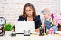 Cheerful young beautiful businesswoman looking at laptop while sitting at her working place with her little daughter Royalty Free Stock Photo