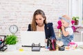 Cheerful young beautiful businesswoman looking at laptop while sitting at her working place with her little daughter Royalty Free Stock Photo