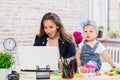 Cheerful young beautiful businesswoman looking at laptop while sitting at her working place with her little daughter Royalty Free Stock Photo