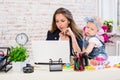 Cheerful young beautiful businesswoman looking at laptop while sitting at her working place with her little daughter Royalty Free Stock Photo