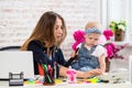 Cheerful young beautiful businesswoman looking at telephone while sitting at her working place with her little daughter Royalty Free Stock Photo