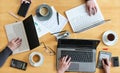 Working together on a joint business project, top view of the wooden table with hands, three laptops, papers, calculator and