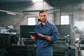 Working by using digital tablet. Man at the factory that is in blue uniform is indoors Royalty Free Stock Photo