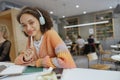 A working woman in headphones sits at a table with a pen in hand, smiling in a cozy minimalistic cafe Royalty Free Stock Photo
