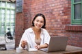 Working woman sitting in coworking space, drinking coffee and using laptop, wearing wireless headphones, watching video Royalty Free Stock Photo