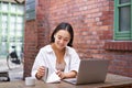 Working woman sitting in coworking space, drinking coffee and using laptop, wearing wireless headphones, watching video Royalty Free Stock Photo