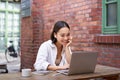 Working woman sitting in coworking space, drinking coffee and using laptop, wearing wireless headphones, watching video Royalty Free Stock Photo