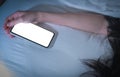 Working woman sleeping in bed at home and hand holding blank screen mobile phone. Woman using smartphone in bedroom. Royalty Free Stock Photo