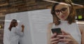 Working woman in white blouse writing on whiteboard in office, viewing code overlay on smartphone Royalty Free Stock Photo