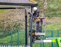 Workman on cherry picker with safety harness painting band stand metalwork in Warminster, Wiltshire, UK