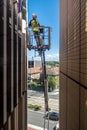 Workman hoisted using a mechanical crane to a high level to inspect shade panels