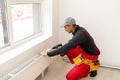 Workman mounting water heating radiator near the window in the white renovated living room, Image with copy space