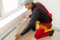 Workman mounting water heating radiator near the window in the white renovated living room, Image with copy space