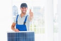 Workman with solar panel gesturing thumbs up in bright office Royalty Free Stock Photo